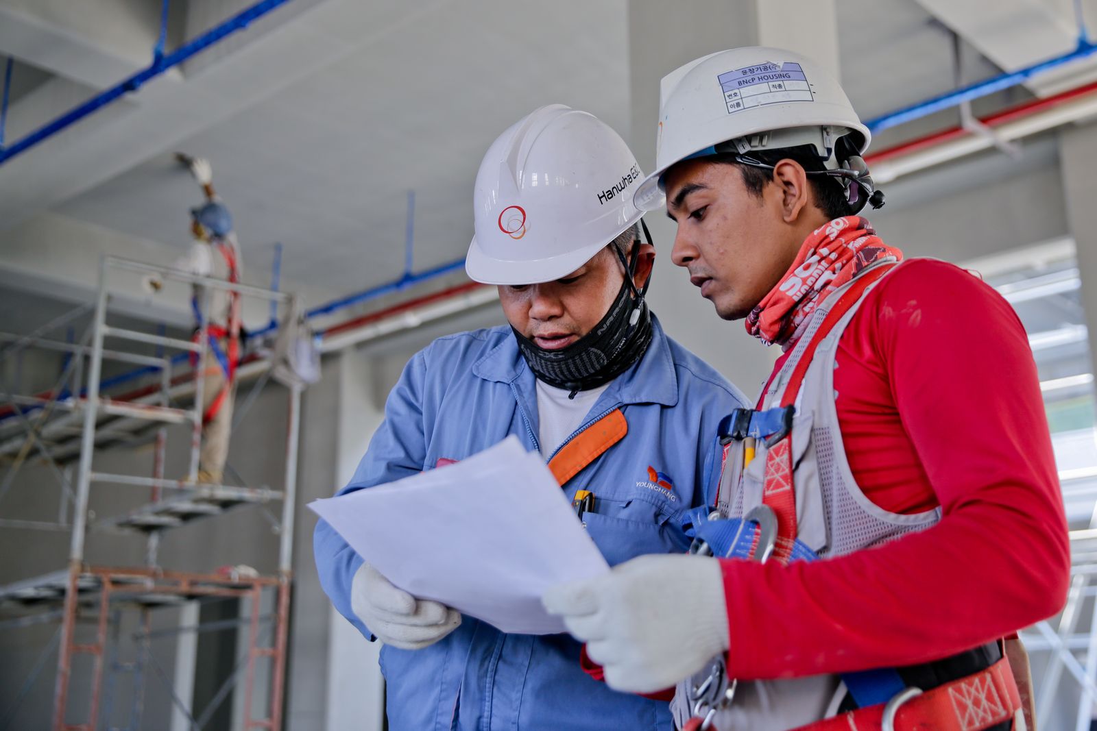 Two site workers in hard hats reviewing construction drawings on site